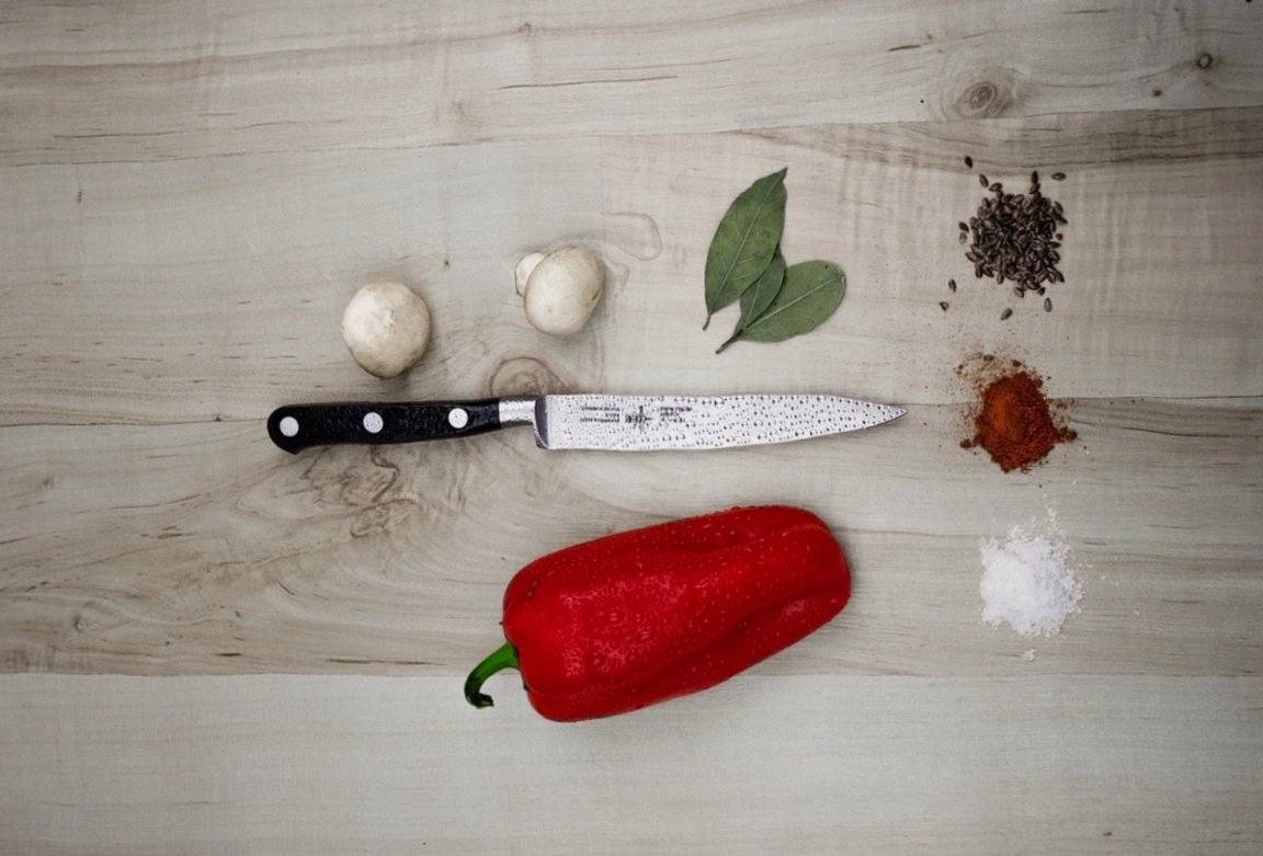 A hand-built chef knife on a wooden bench next to a batch card